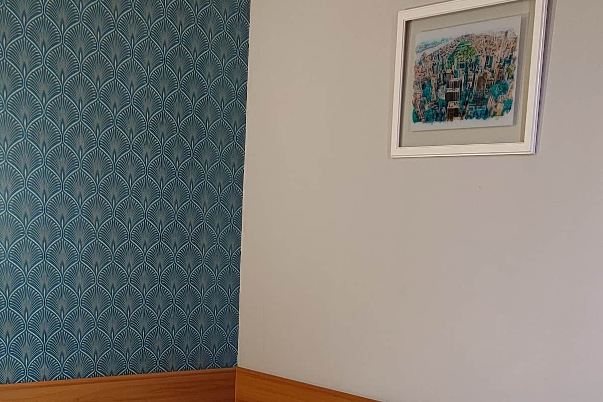 A neatly made bed with white linens and folded towels, a wooden headboard, a patterned teal wall, and a framed picture on the wall.