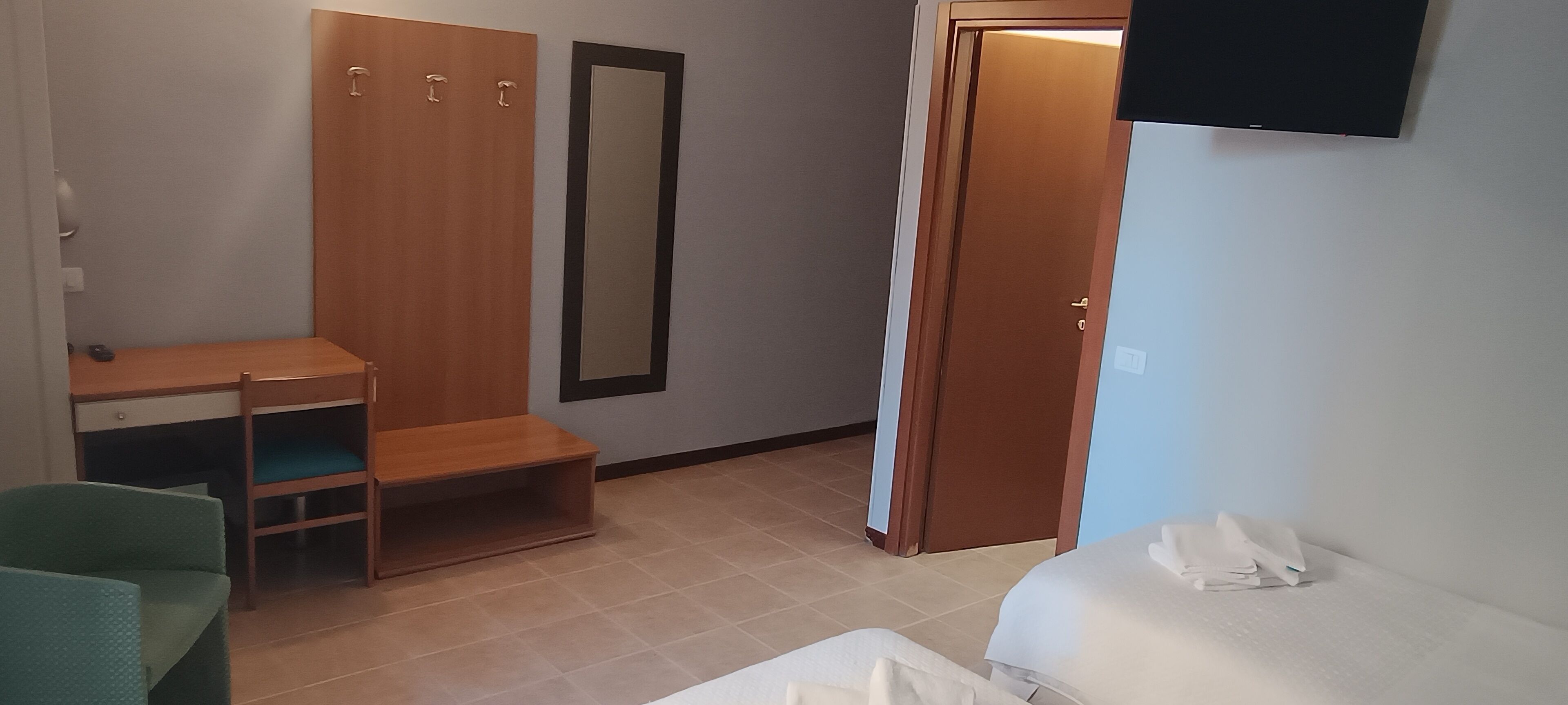 Un dormitorio con cama, escritorio, silla, armario y espejo.