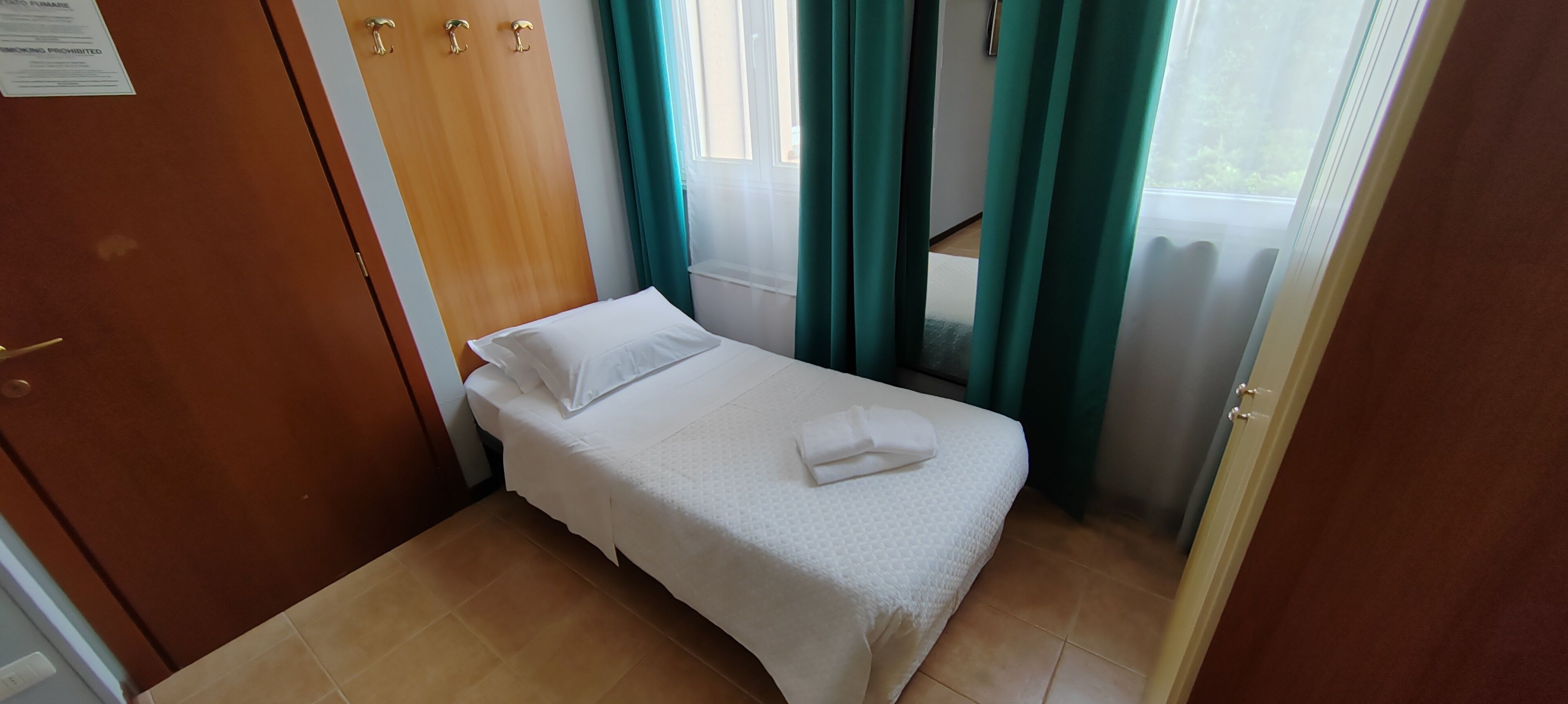 A small, neatly made bed with white bedding in a room with a wooden door and teal curtains.