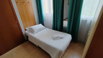 A small, neatly made bed with white bedding in a room with a wooden door and teal curtains.