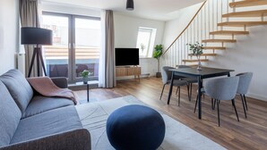 Una sala de estar moderna con un sofá, reposapiés, mesa de comedor, sillas, televisor y una escalera.