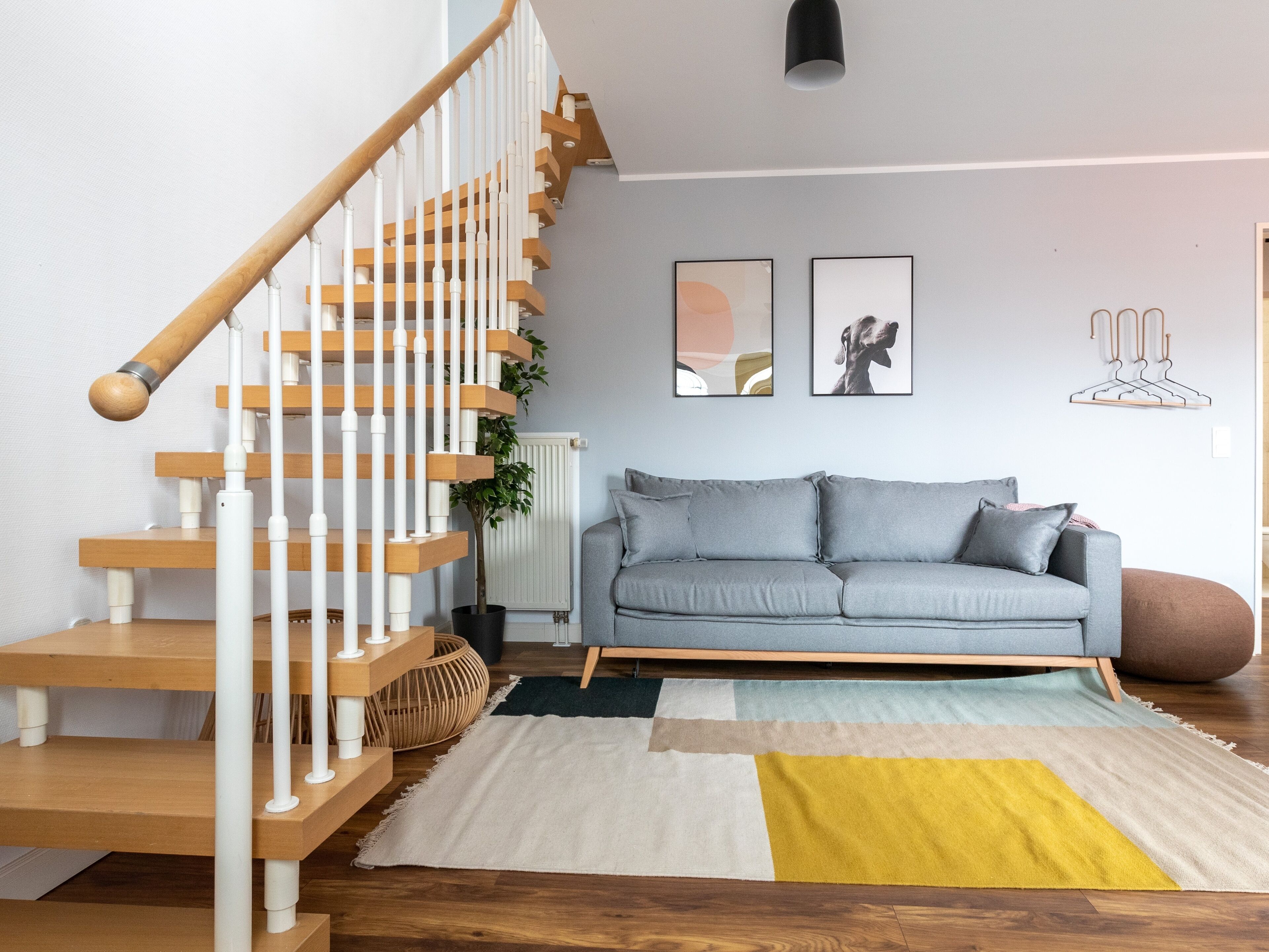 A modern living room with a wooden staircase, grey sofa, and abstract wall art.