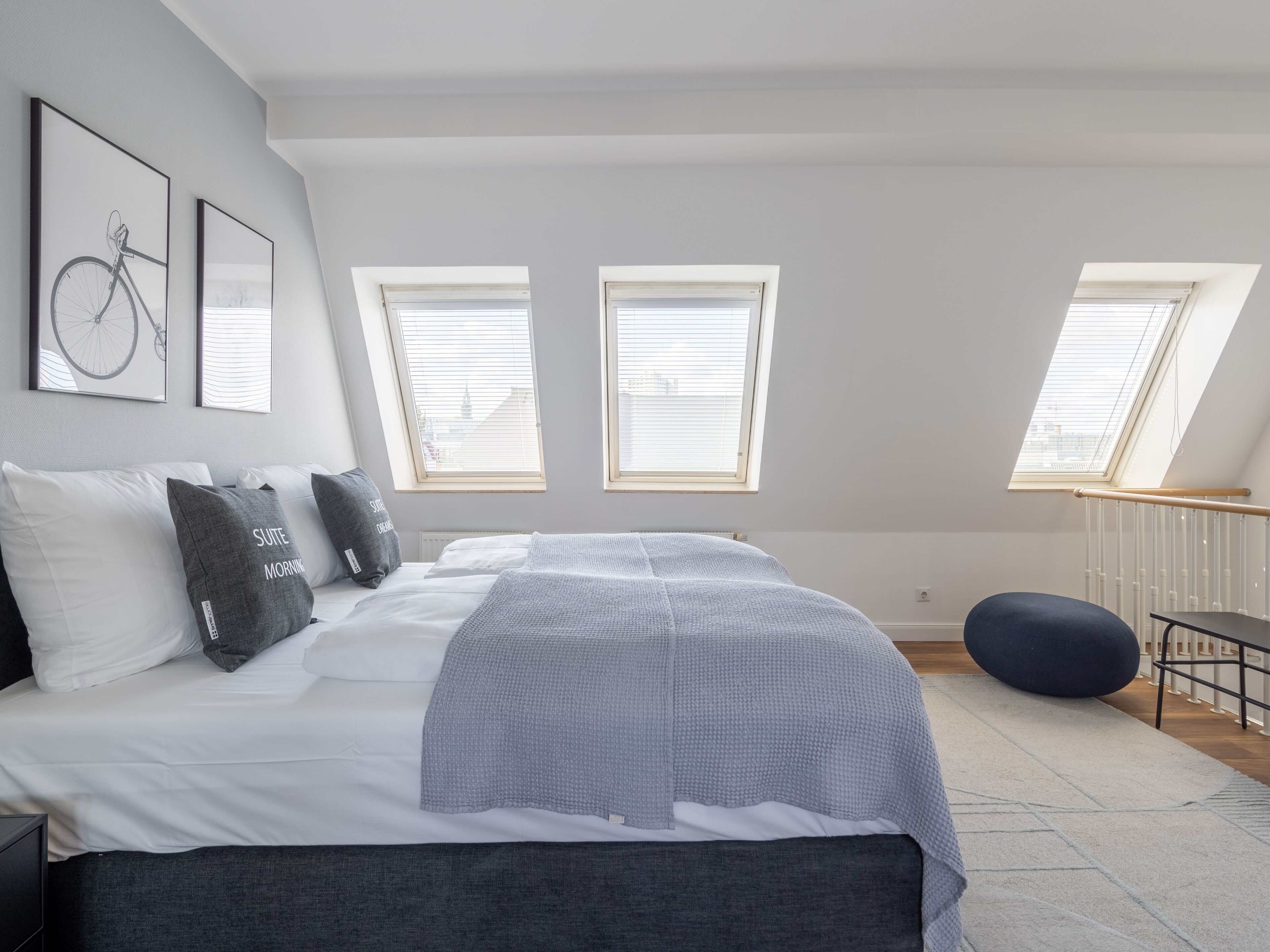 Un dormitorio moderno con una cama grande, dos ventanas con persianas, un tragaluz y vistas a la ciudad.