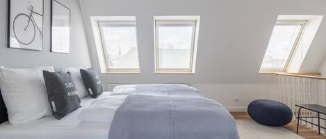 Un dormitorio moderno con una cama grande, dos ventanas con persianas, un tragaluz y vistas a la ciudad.
