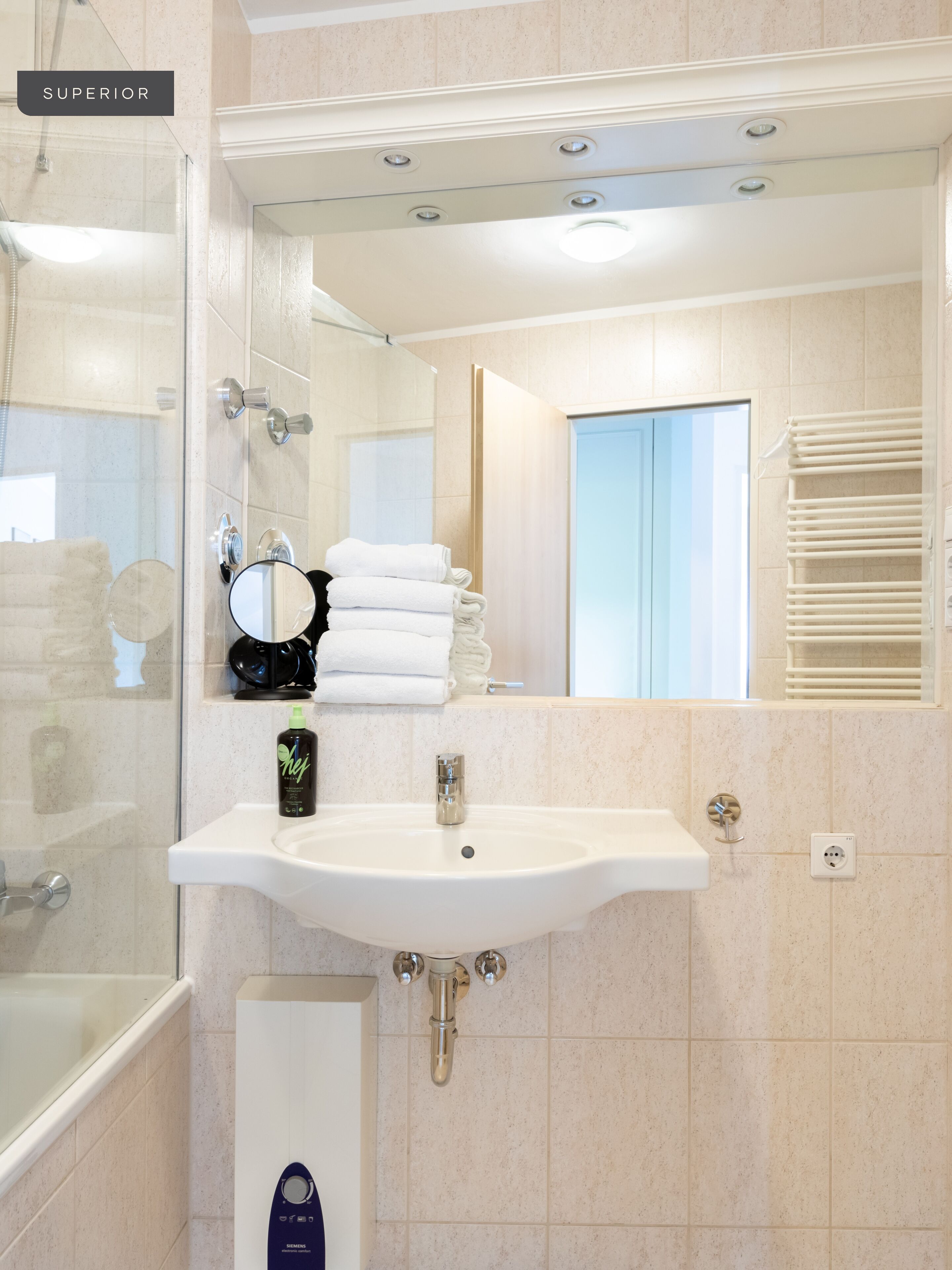 Uma casa de banho moderna com cabine de duche em vidro, lavatório branco com espelho e um porta-toalhas.