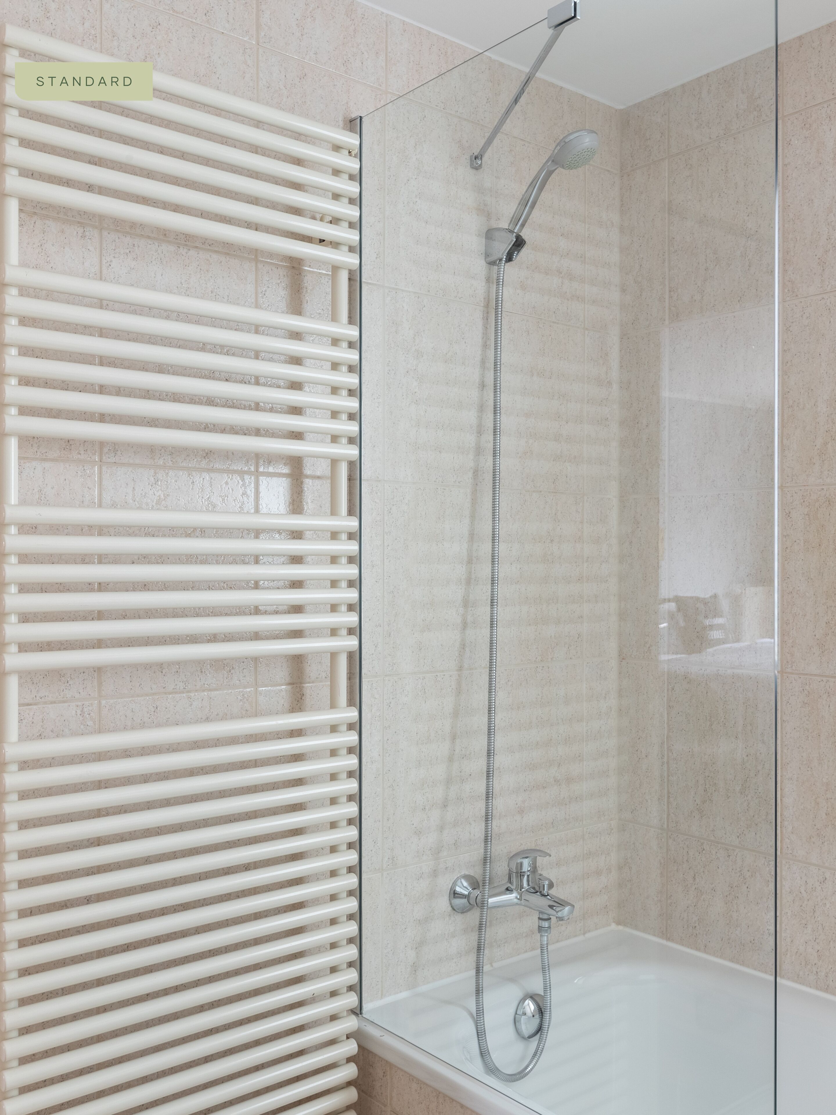 Ein modernes Badezimmer mit einer gläsernen Dusche, einer weißen Badewanne und einem Handtuchhalter mit horizontalen Stangen.