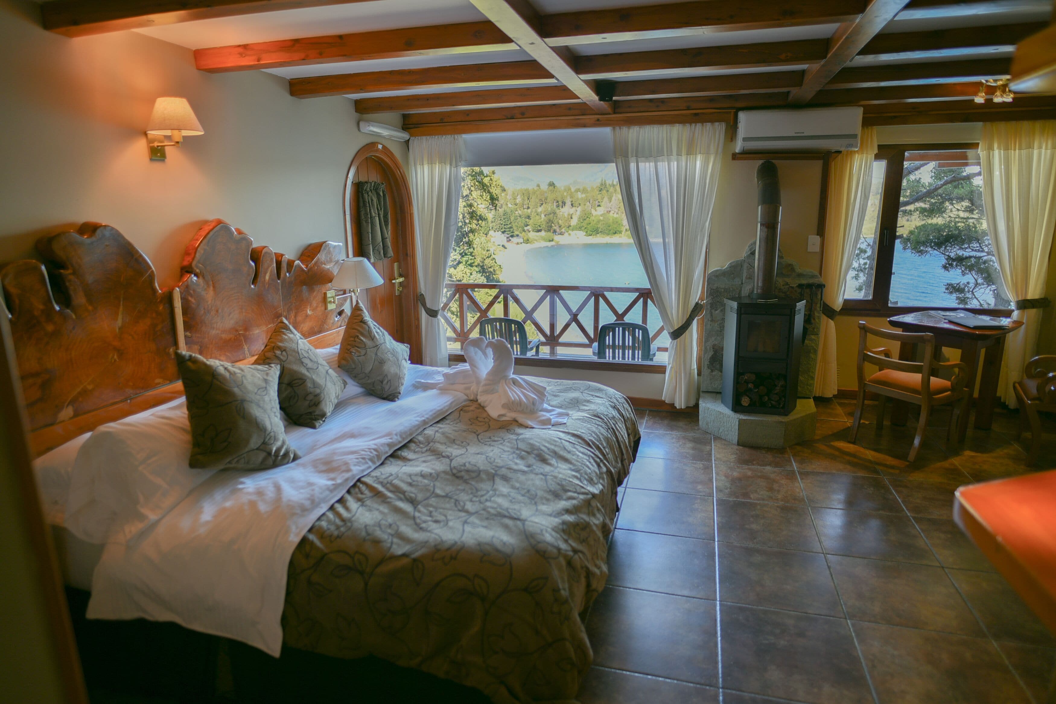 Un dormitorio con una cama grande, cabecera de madera, chimenea y vista a un lago.