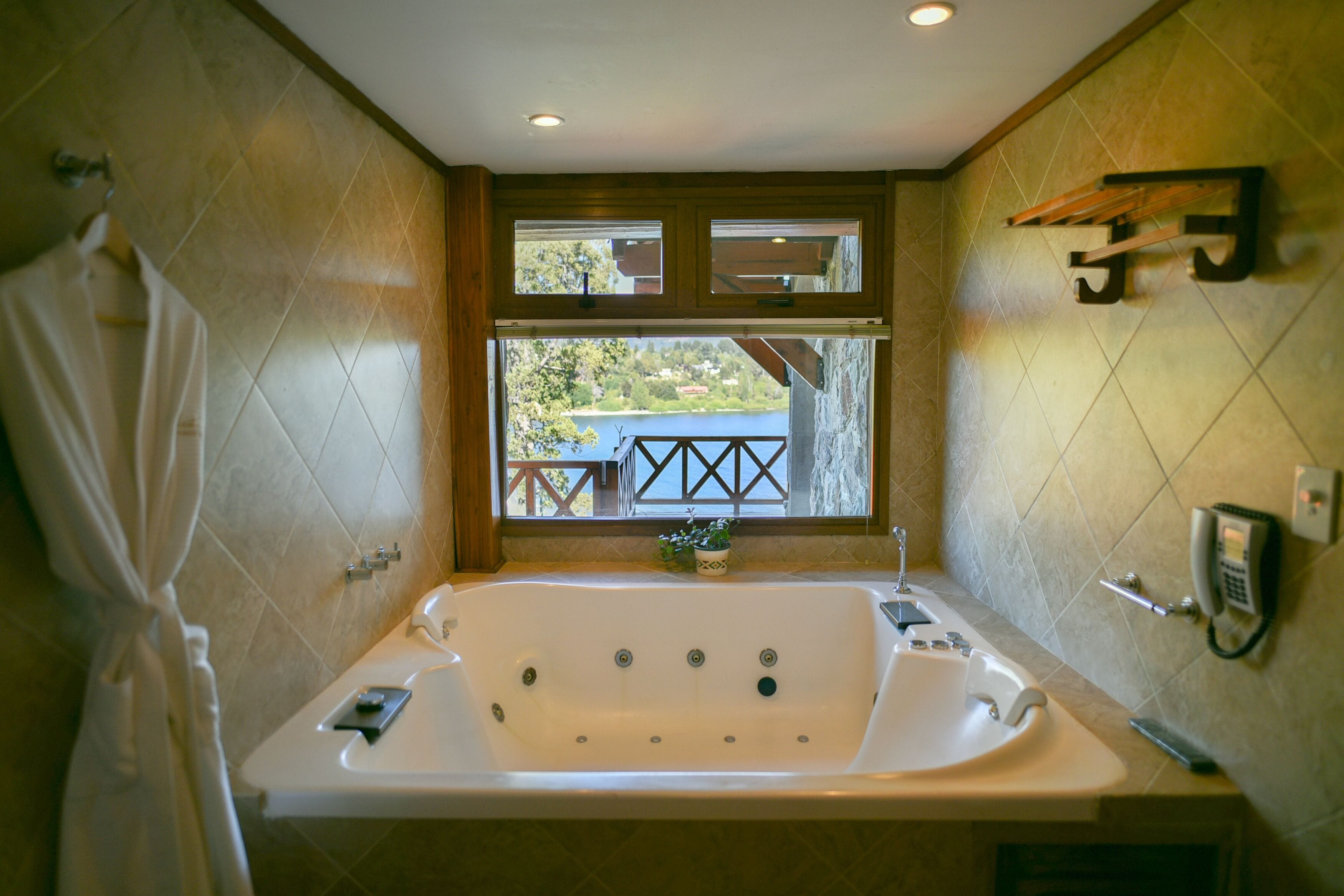Un bagno con una grande vasca da bagno, una finestra con vista su un balcone e un telefono fissato al muro.