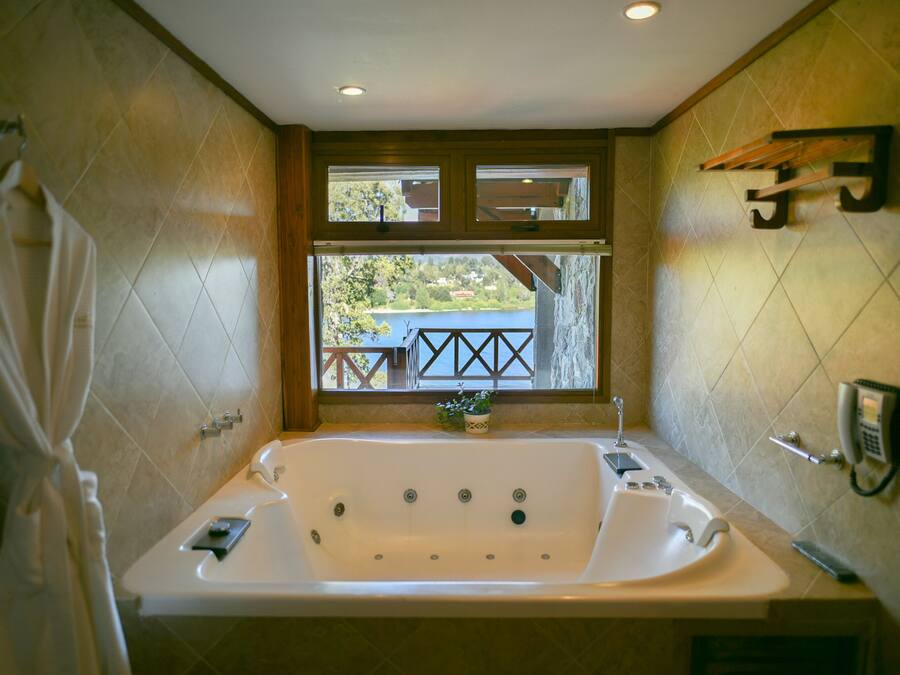 Un bagno con una grande vasca da bagno, una finestra con vista su un balcone e un telefono fissato al muro.