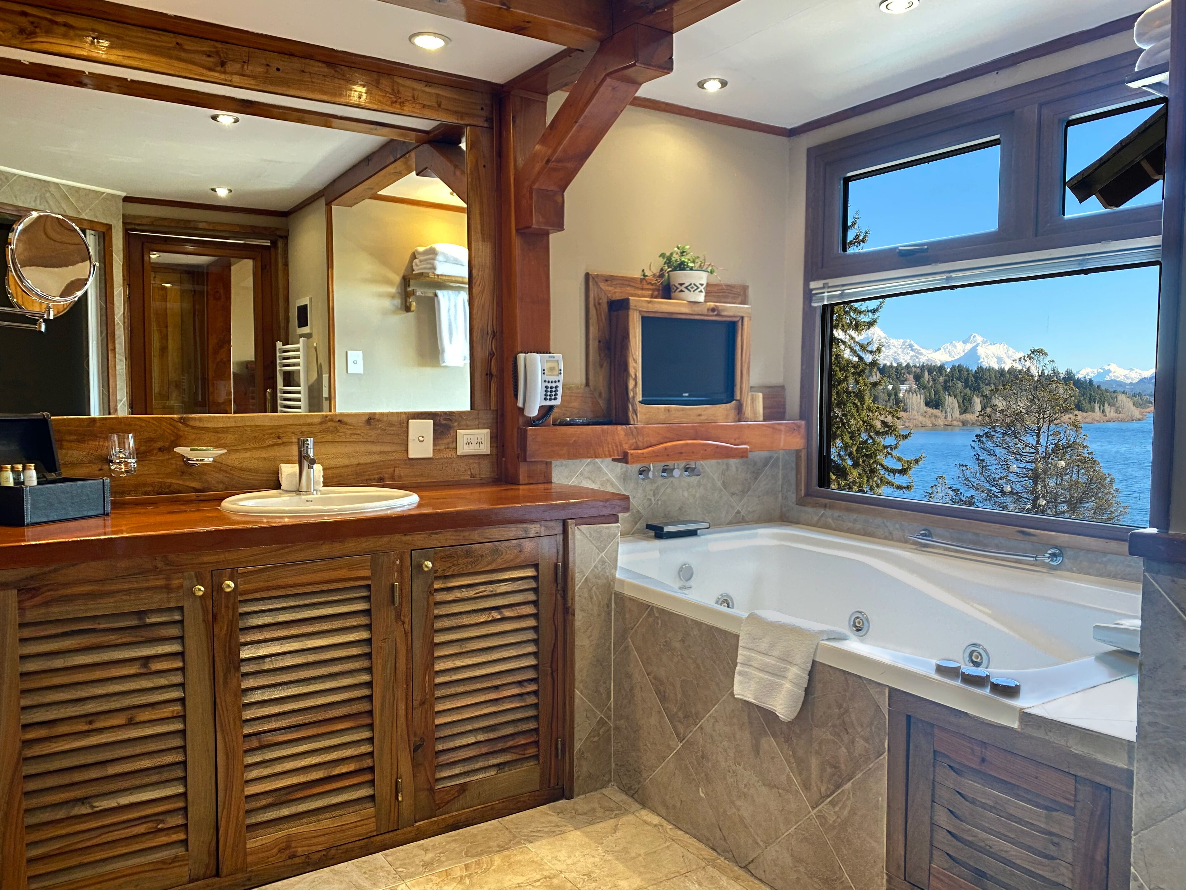 A bathroom with a wooden vanity, a large mirror, a bathtub, and a view of mountains through a window.