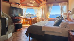 Een slaapkamer met een bed, een televisie, een open haard en uitzicht op bergen en een meer.