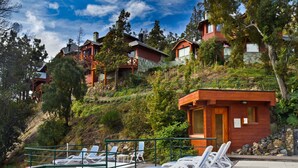 Een resort op een helling met meerdere houten bungalows, een zwembadgedeelte met ligbedden en een klein houten gebouw.