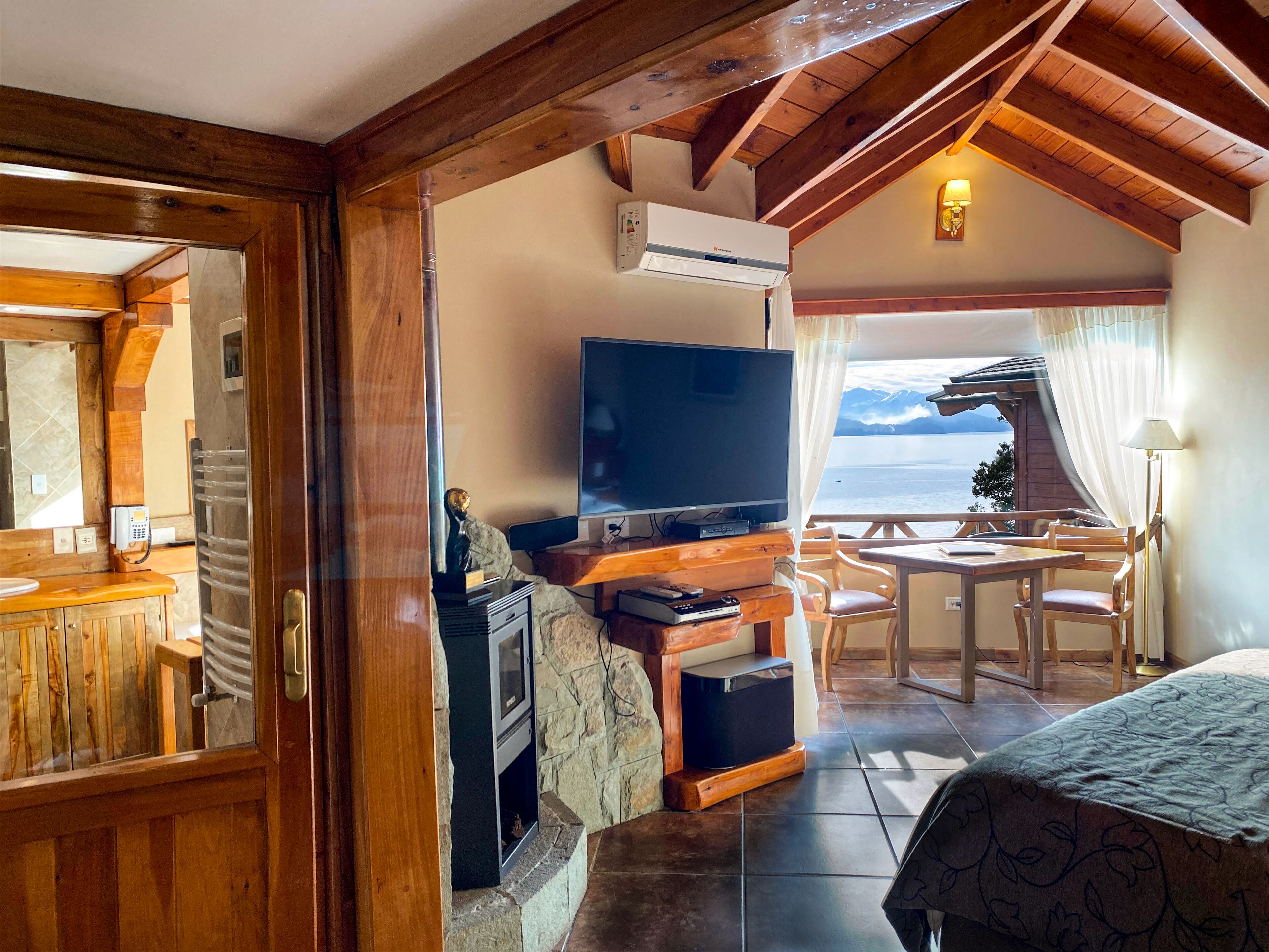 Una habitación acogedora con techo de madera, televisor, chimenea de piedra y vistas al mar.