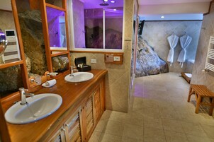 Un baño con dos lavamanos, un espejo grande, ducha con puerta de cristal y un banco de madera.