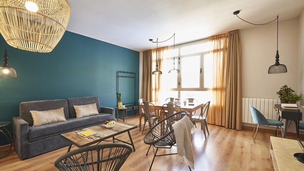 Ein modernes Wohnzimmer mit einer Couch, einem Esstisch, Stühlen und einem großen Fenster mit Vorhängen.