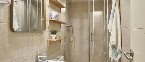 A modern bathroom with a glass-enclosed shower, a sink with a mirror, and wooden shelves with toiletries.