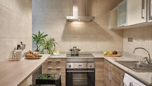 Eine moderne Küche mit Einbauofen, Edelstahl-Spüle und einer großen Kochinsel mit Kaffeemaschine und Croissants.