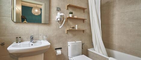Ein modernes Badezimmer mit Waschbecken, Toilette und Badewanne. Holzregale mit Toilettenartikeln und eine hängende Leuchte sind vorhanden.