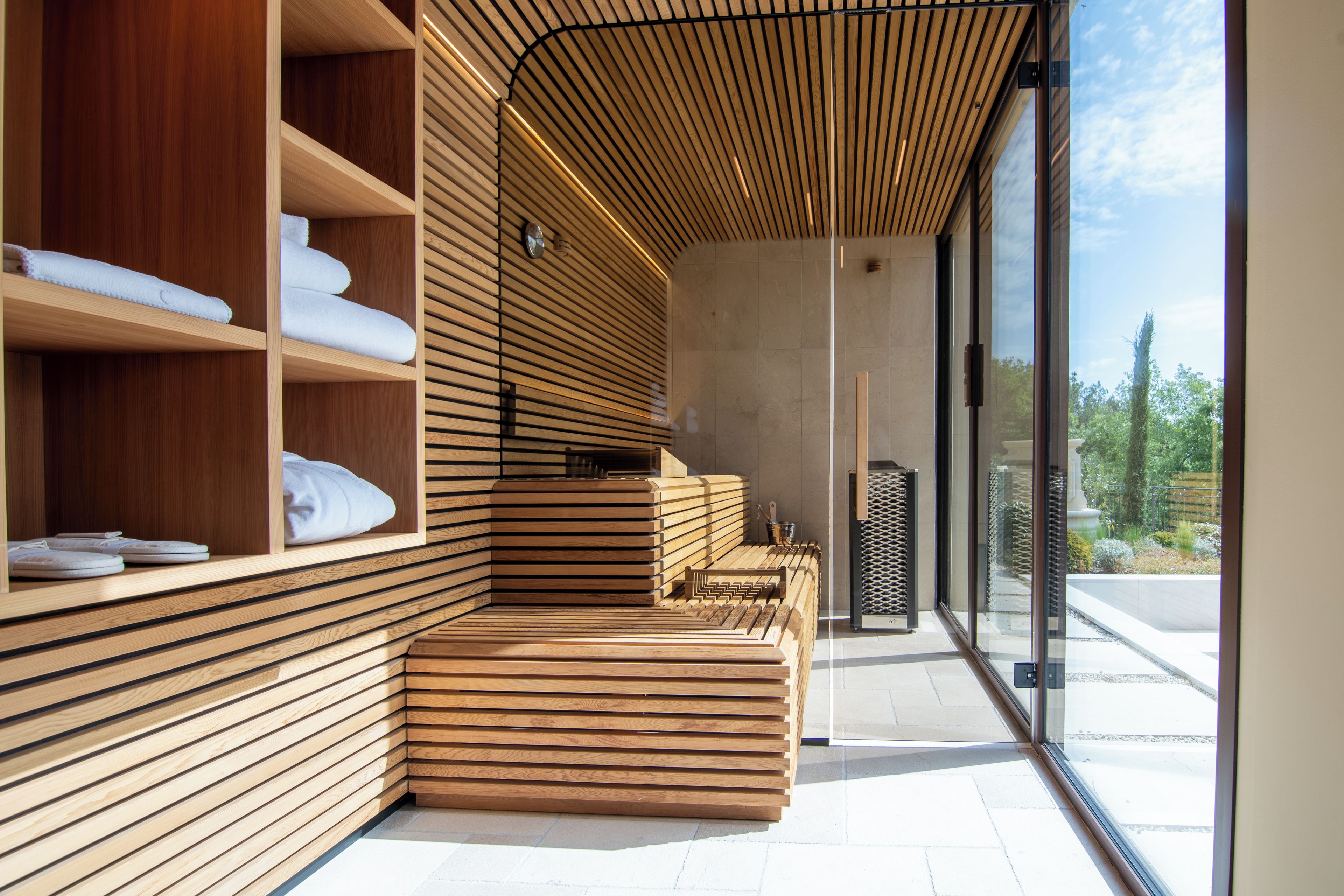 Un spa moderno con paredes de listones de madera, una zona de estar con bancos y vistas al exterior a través de grandes ventanales.