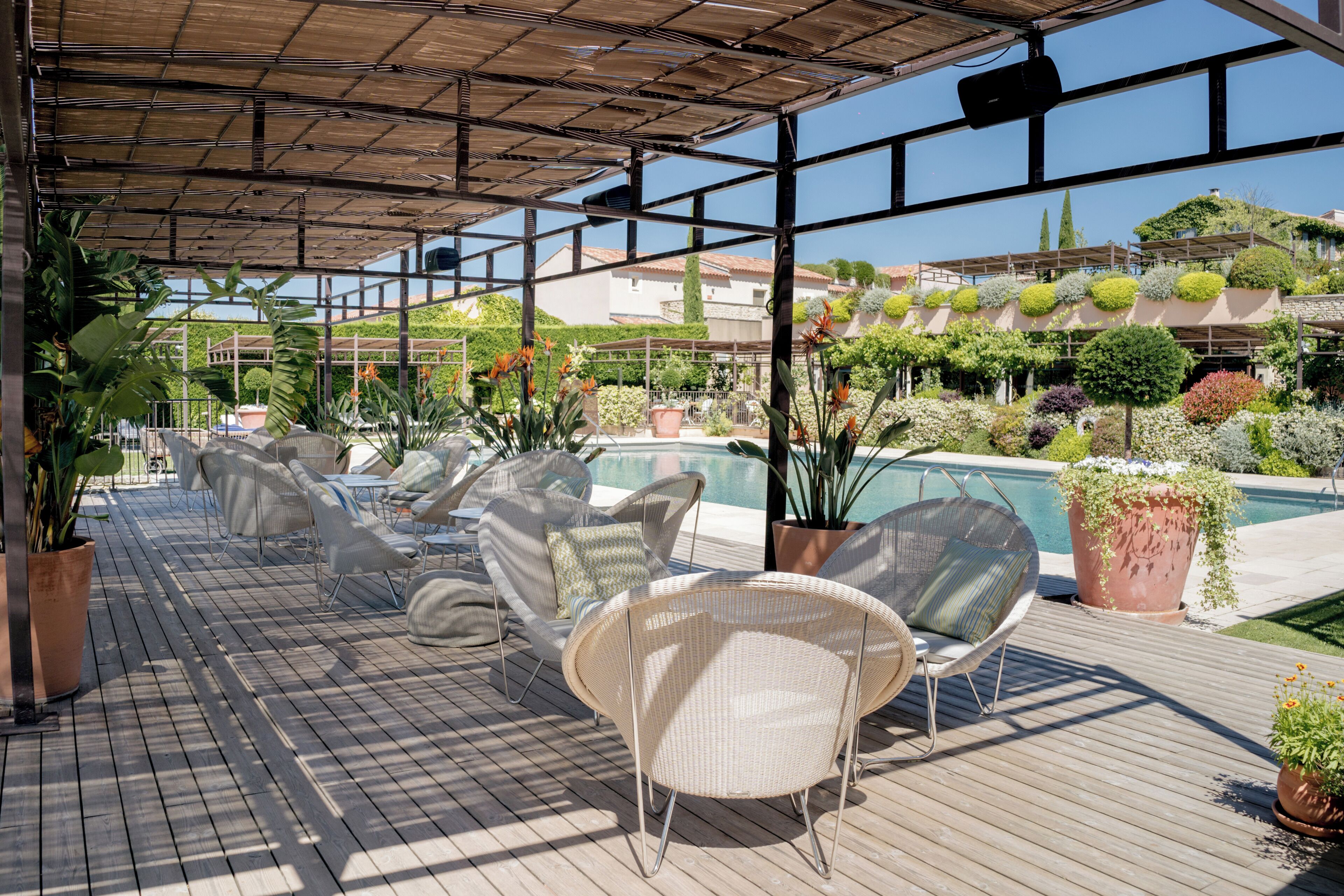 Un espace extérieur aménagé, abrité et doté de chaises en osier et de plantes en pot, offrant une vue sur une piscine et une végétation luxuriante.