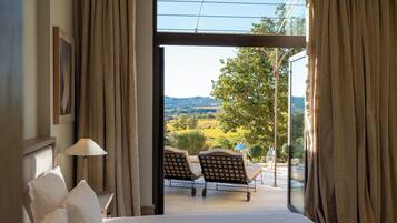 Quarto de hotel com cama grande, vista para o exterior e área de estar com cadeiras e mesa.