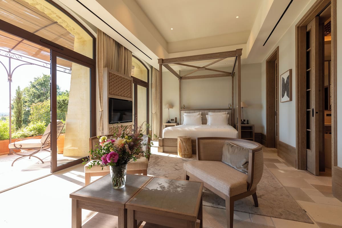 A spacious bedroom with a large bed, a sitting area, and a balcony with outdoor furniture.