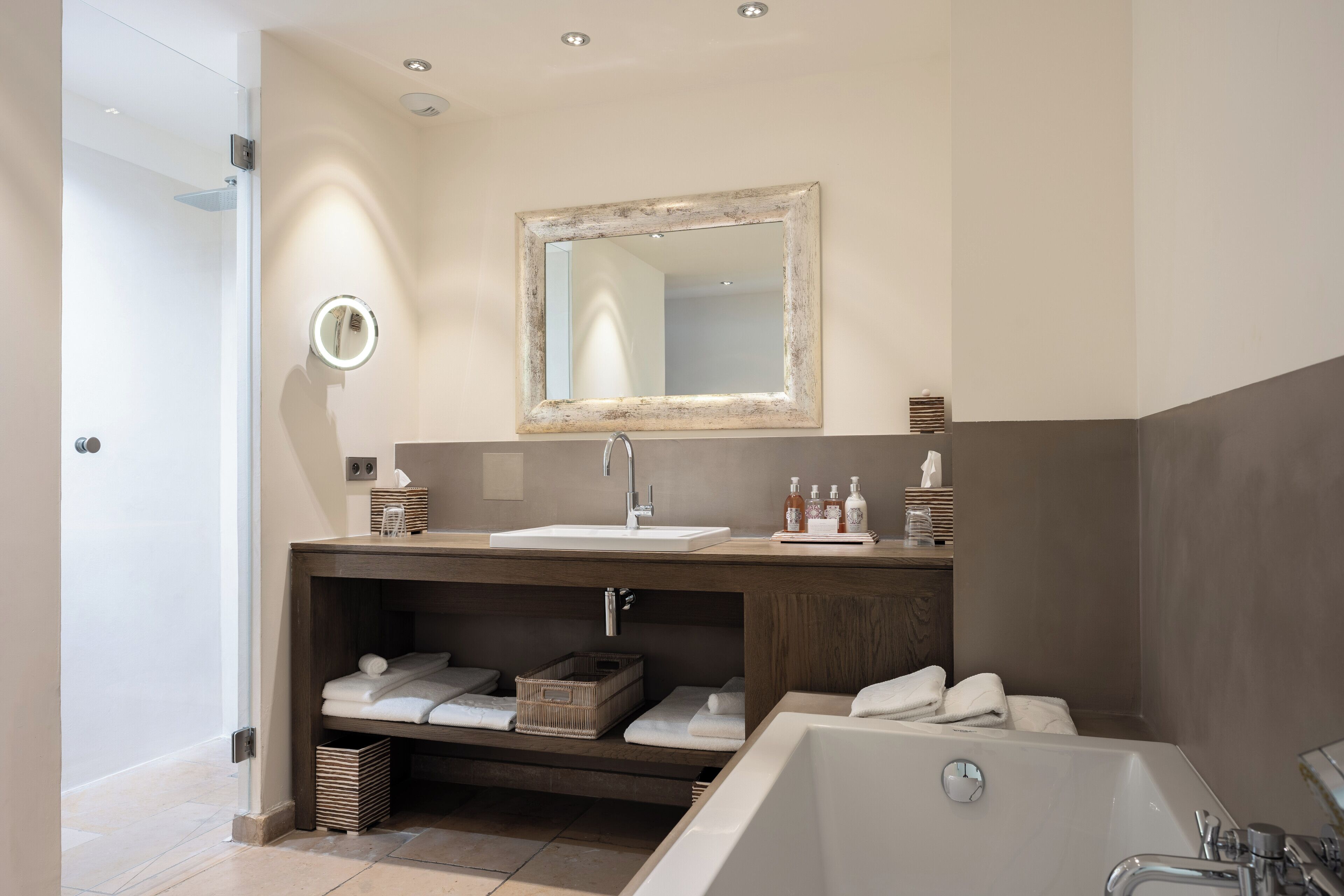 Un baño moderno con tocador de madera, un espejo grande, una bañera y toallas ordenadas.