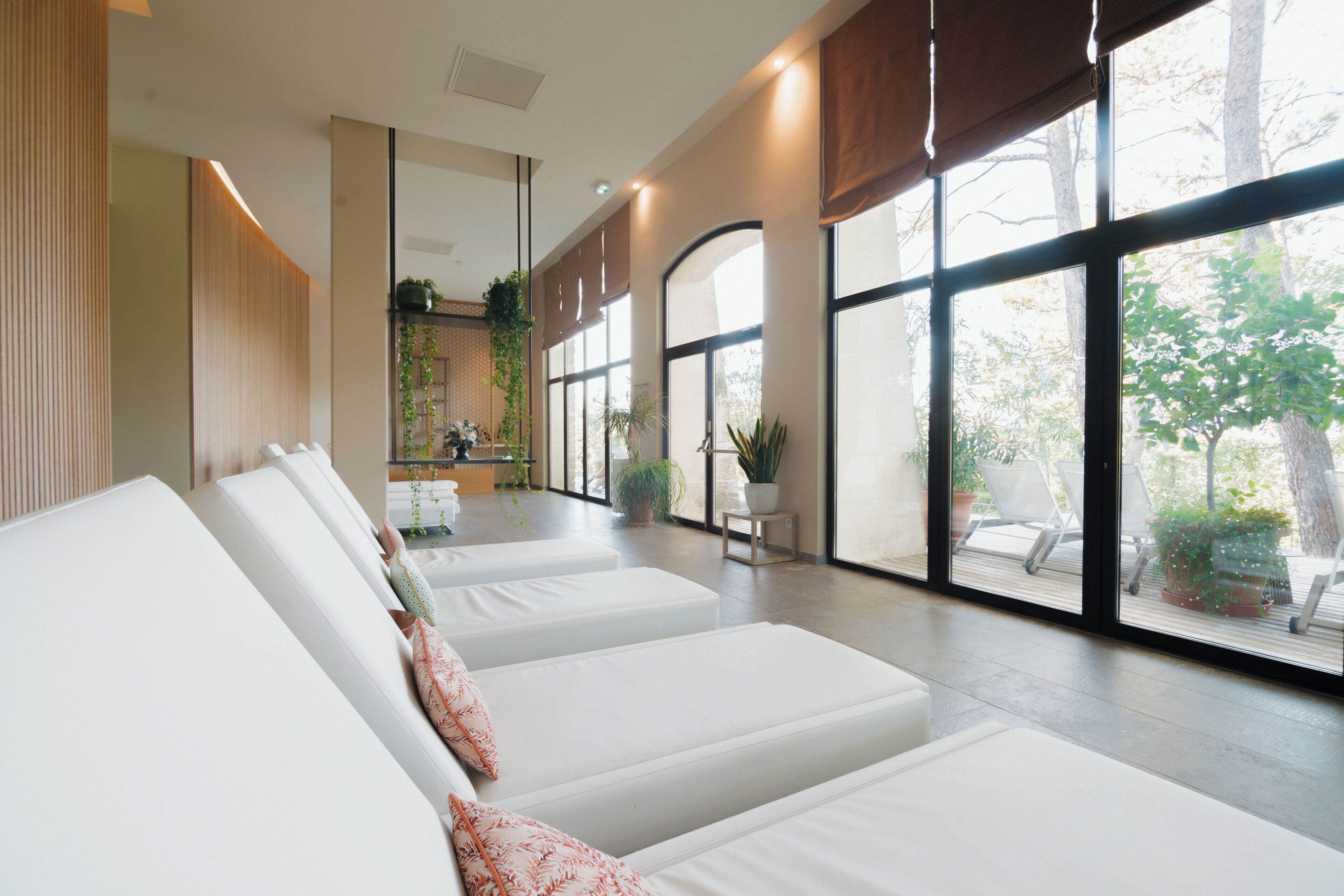 A modern spa room with white lounge chairs, large windows, and indoor plants.