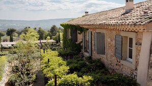 A rustic stone house with a tiled roof, surrounded by lush greenery and a view of distant hills.