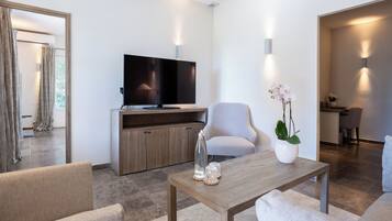 Een moderne woonkamer met een flatscreen televisie, een grijze fauteuil, een houten salontafel en een potorkidee.