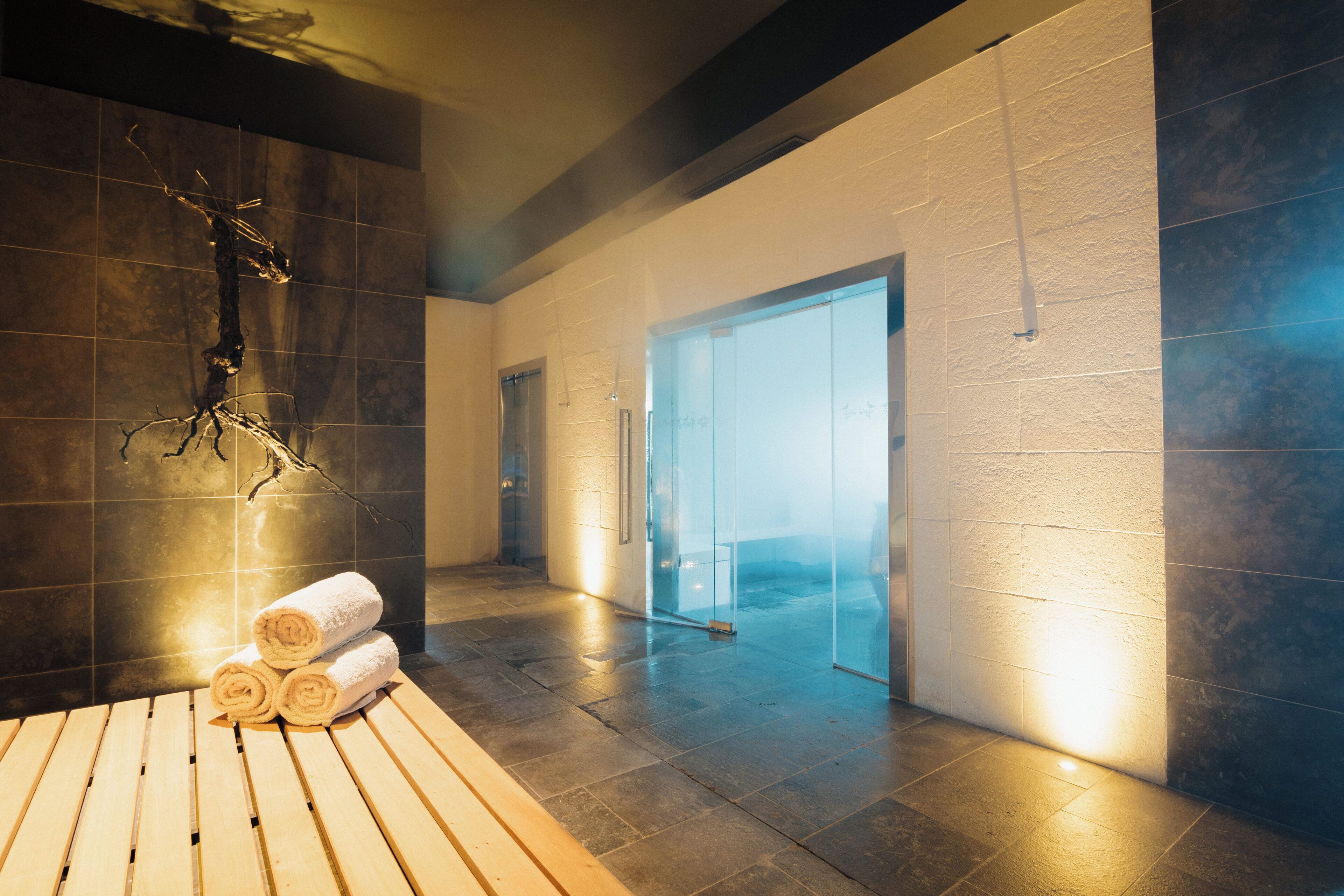 Un área de spa con un banco de madera, toallas enrolladas y una escultura en la pared.