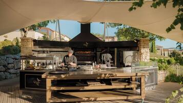 An outdoor kitchen with a large grill, stone pillars, and a canopy.