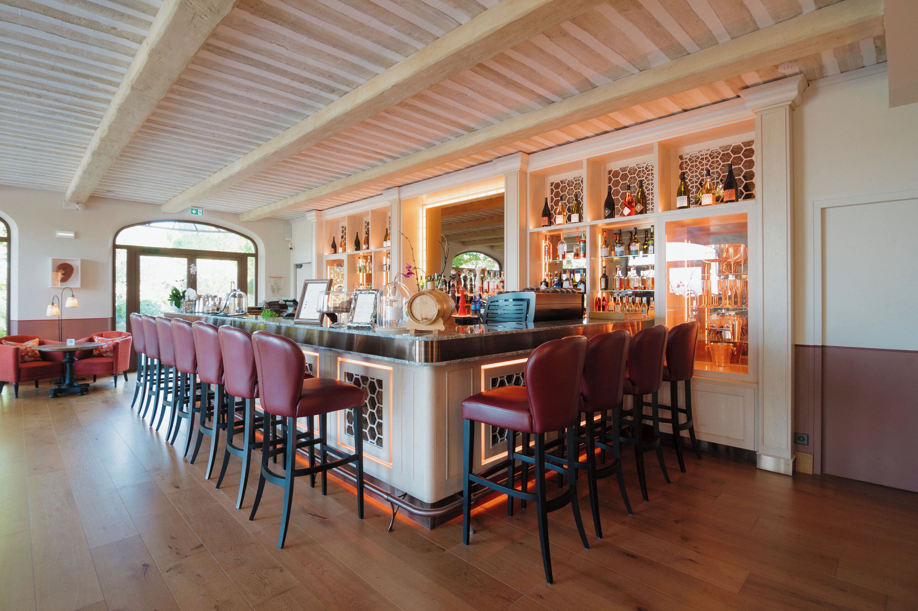A bar area with a long counter, multiple bar stools, and shelves with bottles.