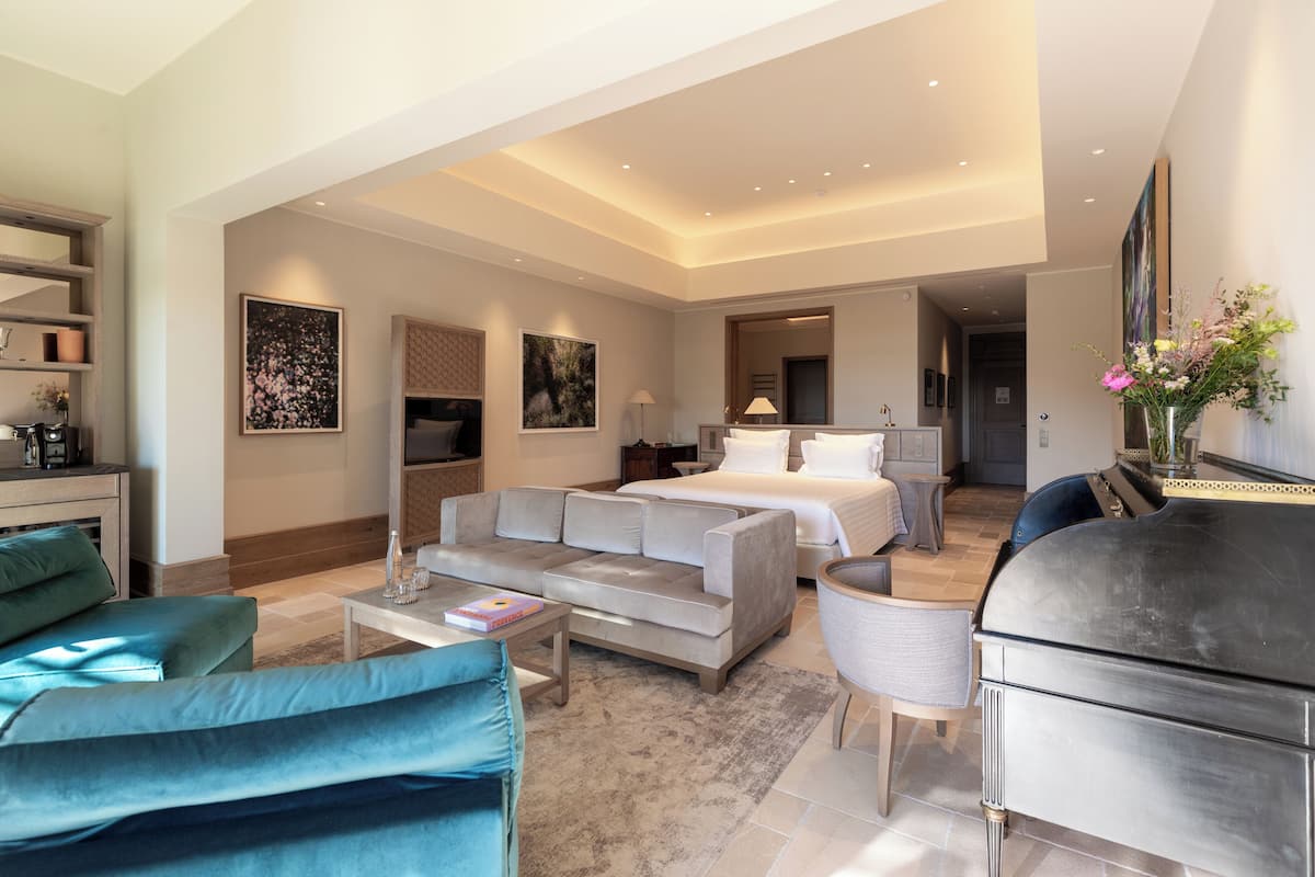 A modern hotel room with a large bed, a sofa, a coffee table, and a piano.