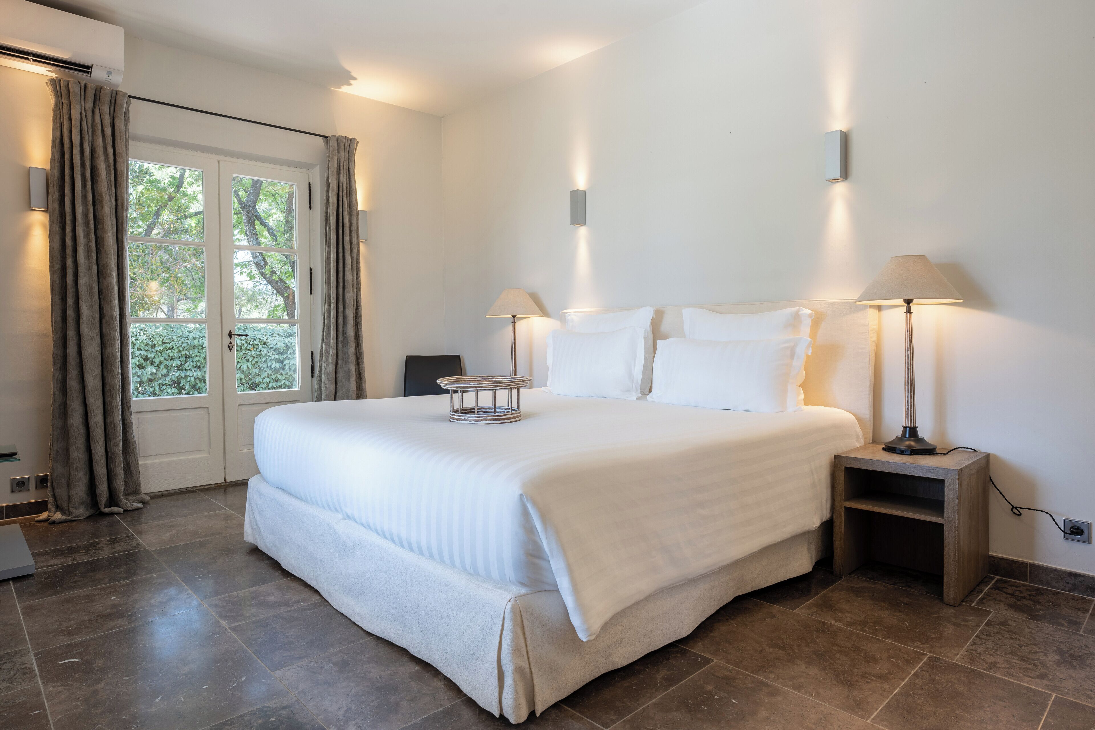 A spacious bedroom with a large bed, two bedside lamps, and a view through a glass door.