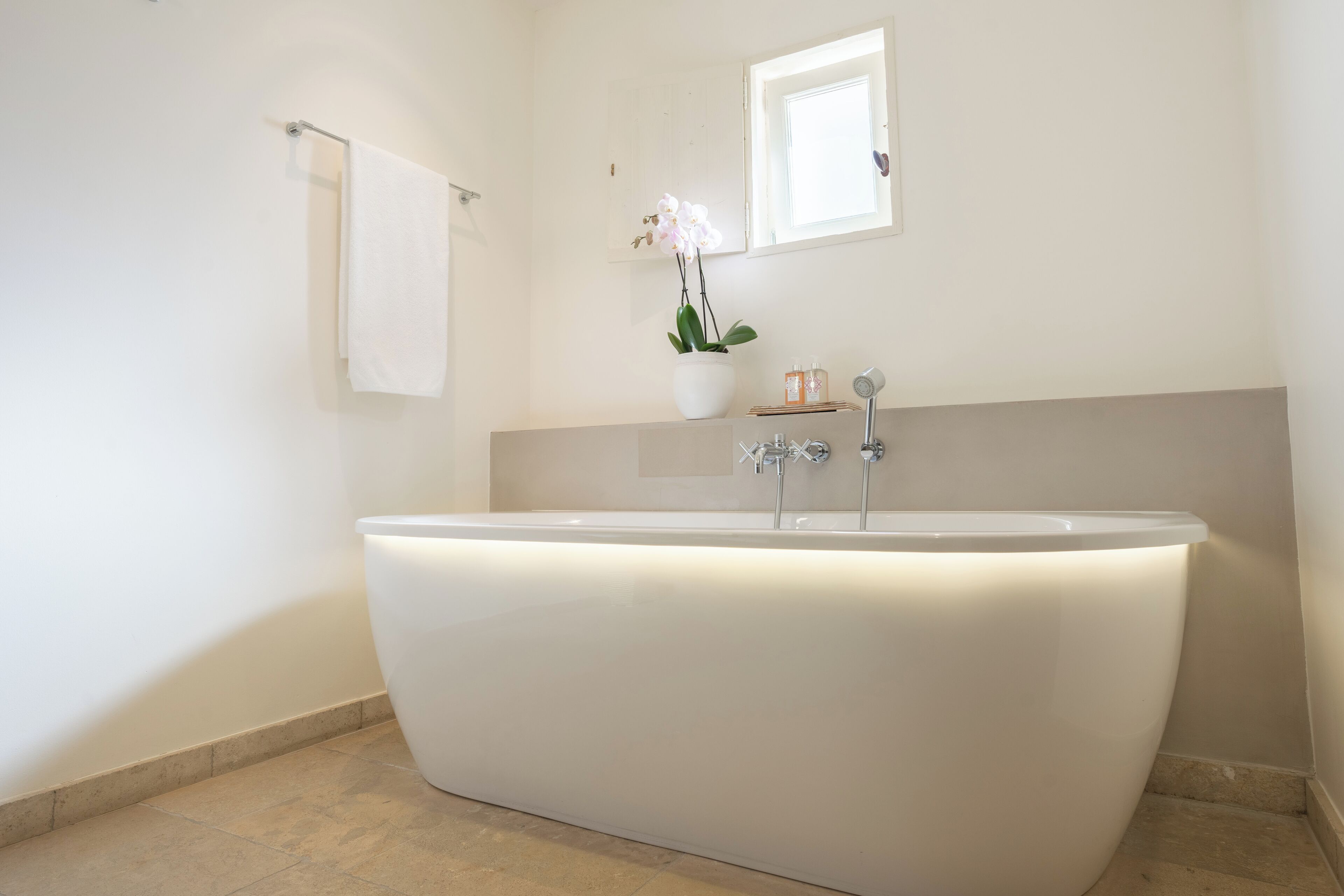 A modern bathroom with a freestanding bathtub, a white sink, and a small window above the mirror.