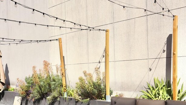 An outdoor seating area with a sofa and benches, string lights, and planters against a concrete wall. - Brit Hotel Essentiel Reims Taissy (Taissy)