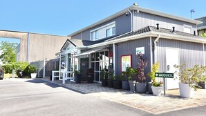 A hotel with a covered entrance, potted plants, and a sign indicating the entrance. - Brit Hotel Essentiel Reims Taissy (Taissy)