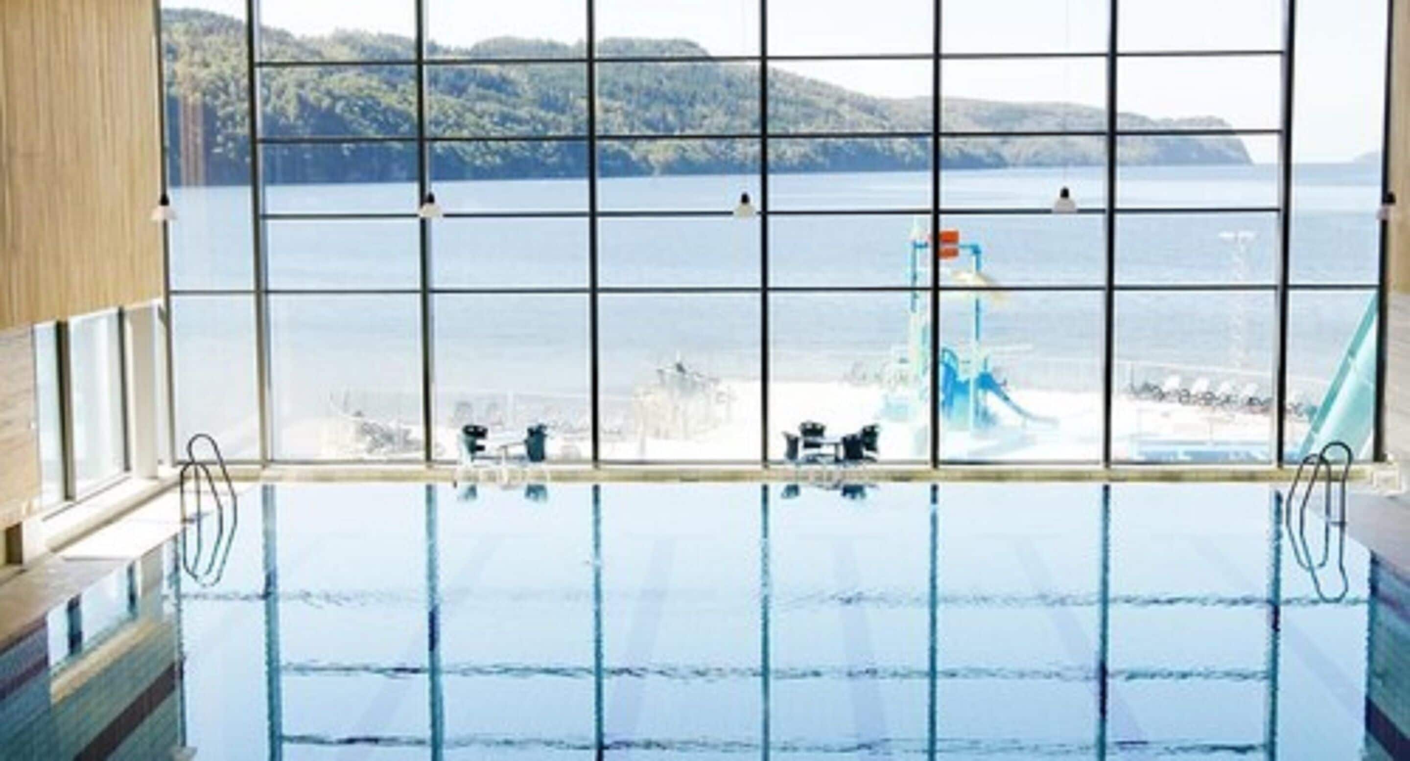 Piscina interna com vista para o mar através de uma grade de janelas.