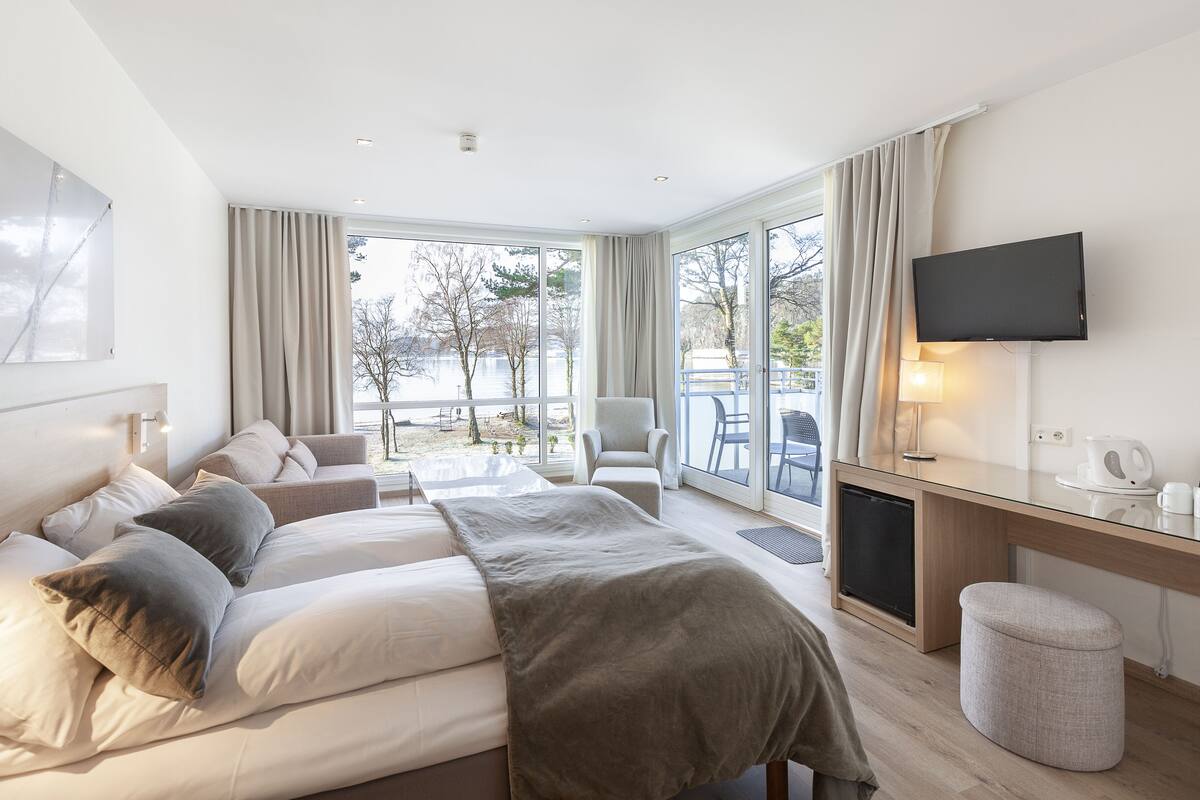 Ein modernes Hotelzimmer mit einem großen Bett, einem Schreibtisch, einem Sessel und einem Fernseher.
