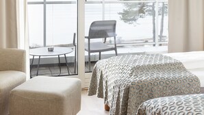 Una habitación con un gran ventanal corredera que da a un balcón con vistas al agua y a los árboles. Hay dos camas con cubrecamas estampados, una silla y una pequeña mesa.