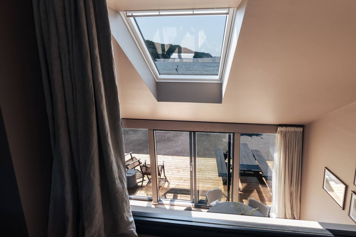 Ein Zimmer mit Dachfenster, großen Fenstern und Blick auf eine Außenterrasse mit Möbeln.