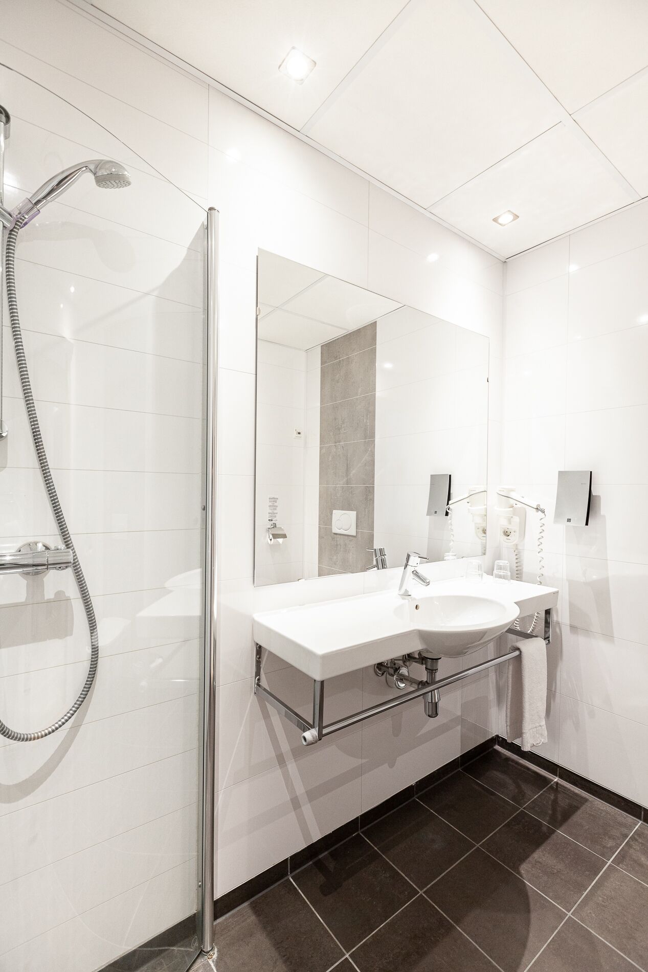 Ein modernes Badezimmer mit einer gläsernen Duschkabine, einem weißen Waschbecken mit Spiegel und einem dunklen Fliesenboden.