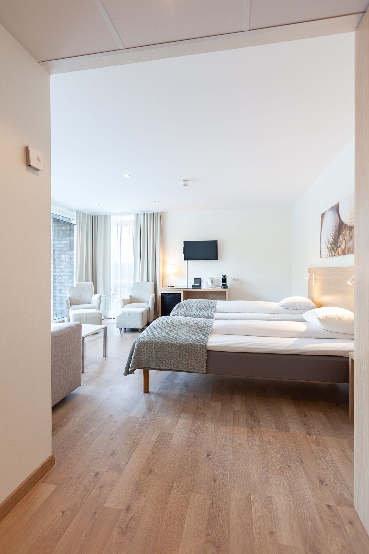 A modern hotel room with a large bed, a desk, a chair, and a TV.