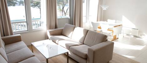 A modern living room with a beige sofa, a white coffee table, and a dining area with a white table and chairs.