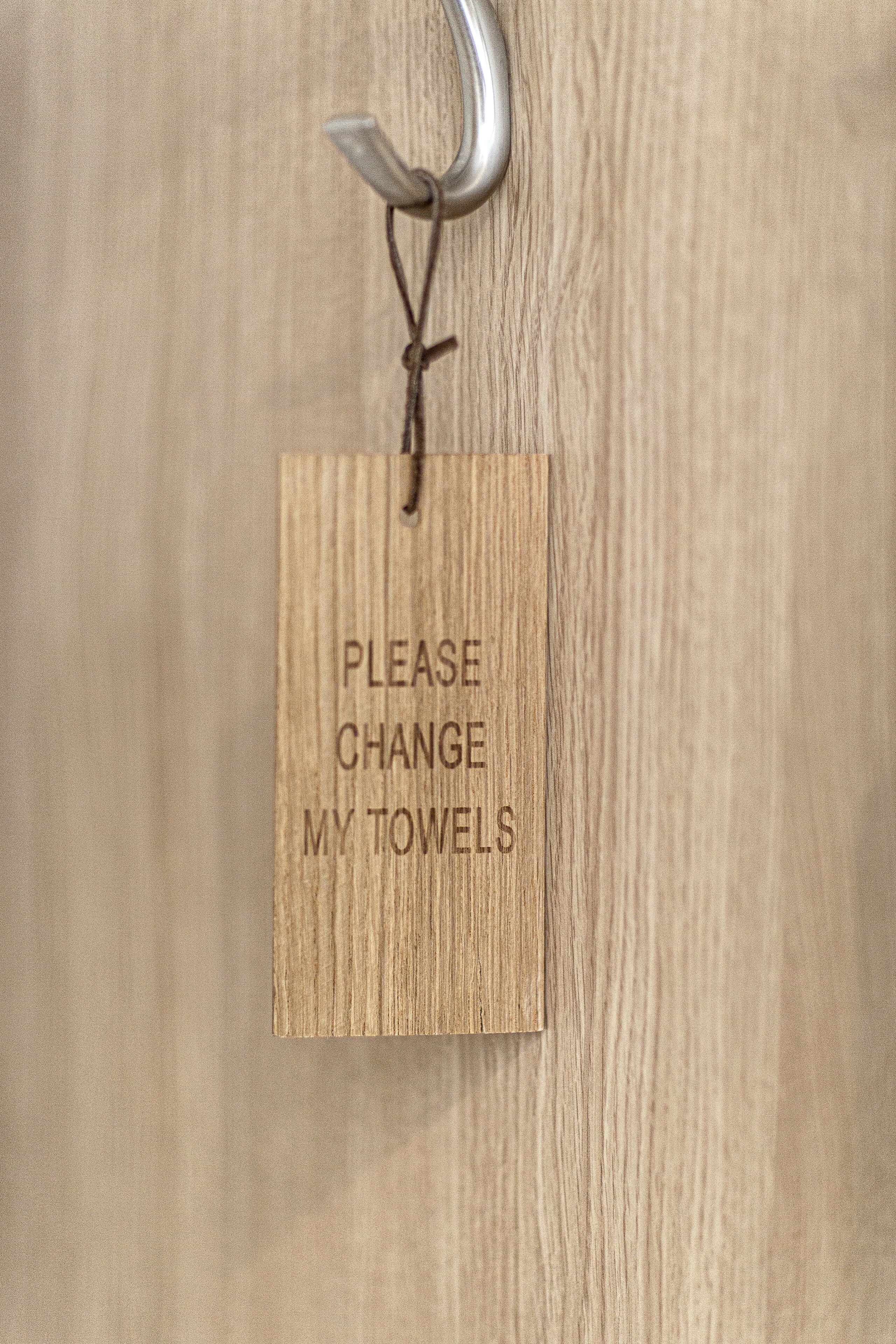 Un letrero de madera con el texto 'POR FAVOR, CAMBIE MIS TOALLAS' colgado en una puerta.