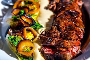 Un plato de carne con cebollas a la parrilla y vegetales verdes.