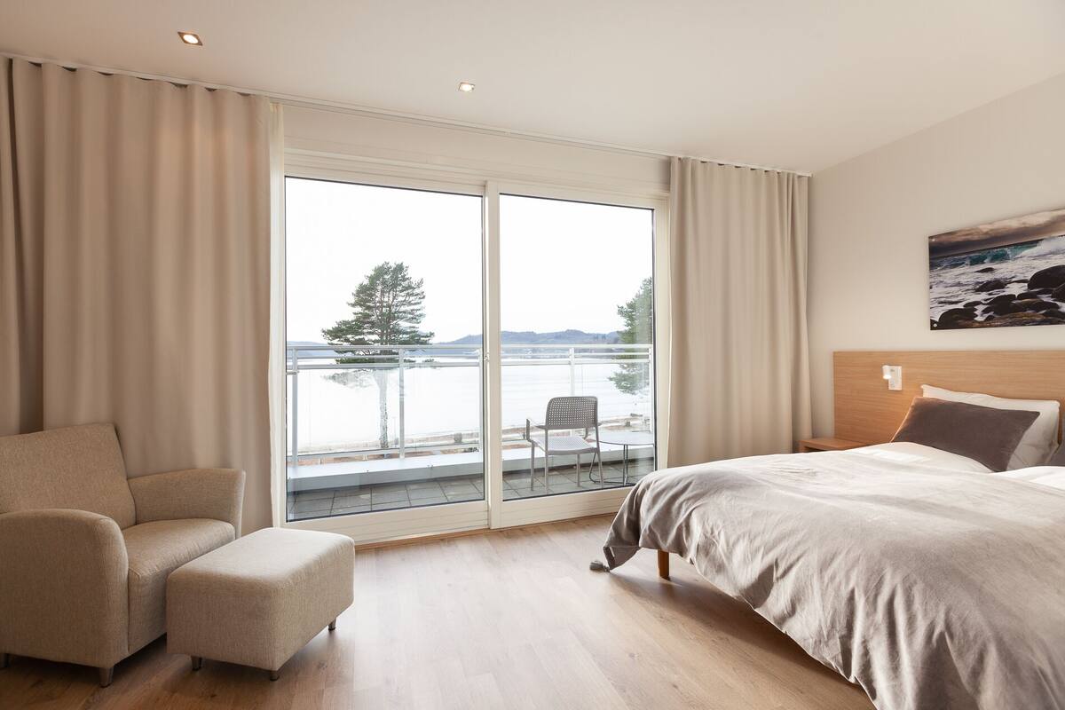 Ein Hotelzimmer mit einer großen Schiebeglastür, die auf einen Balkon führt, einem Bett, einem Sessel und einem kleinen Tisch.