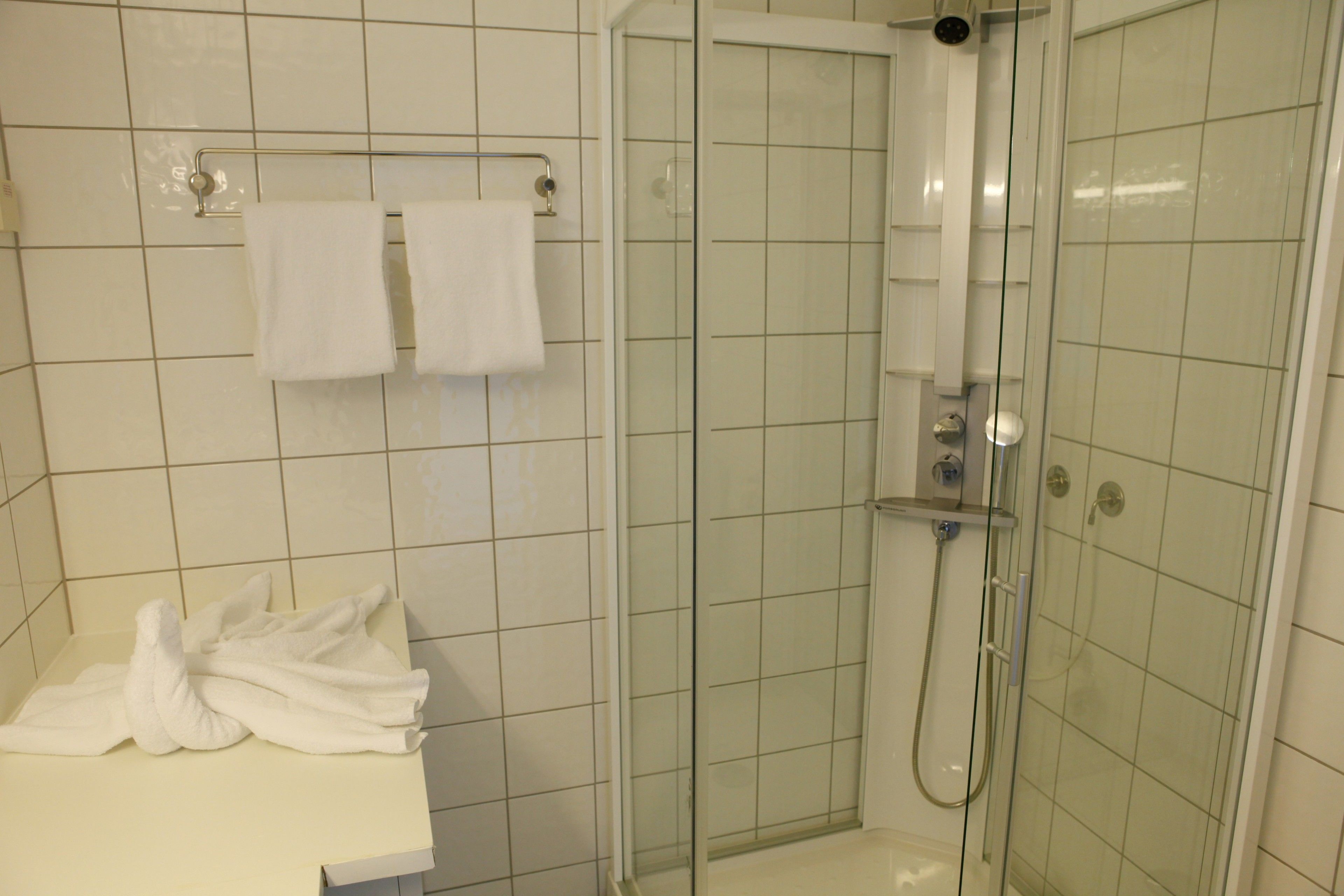 A bathroom with a shower, a sink, and a towel rack with two towels.