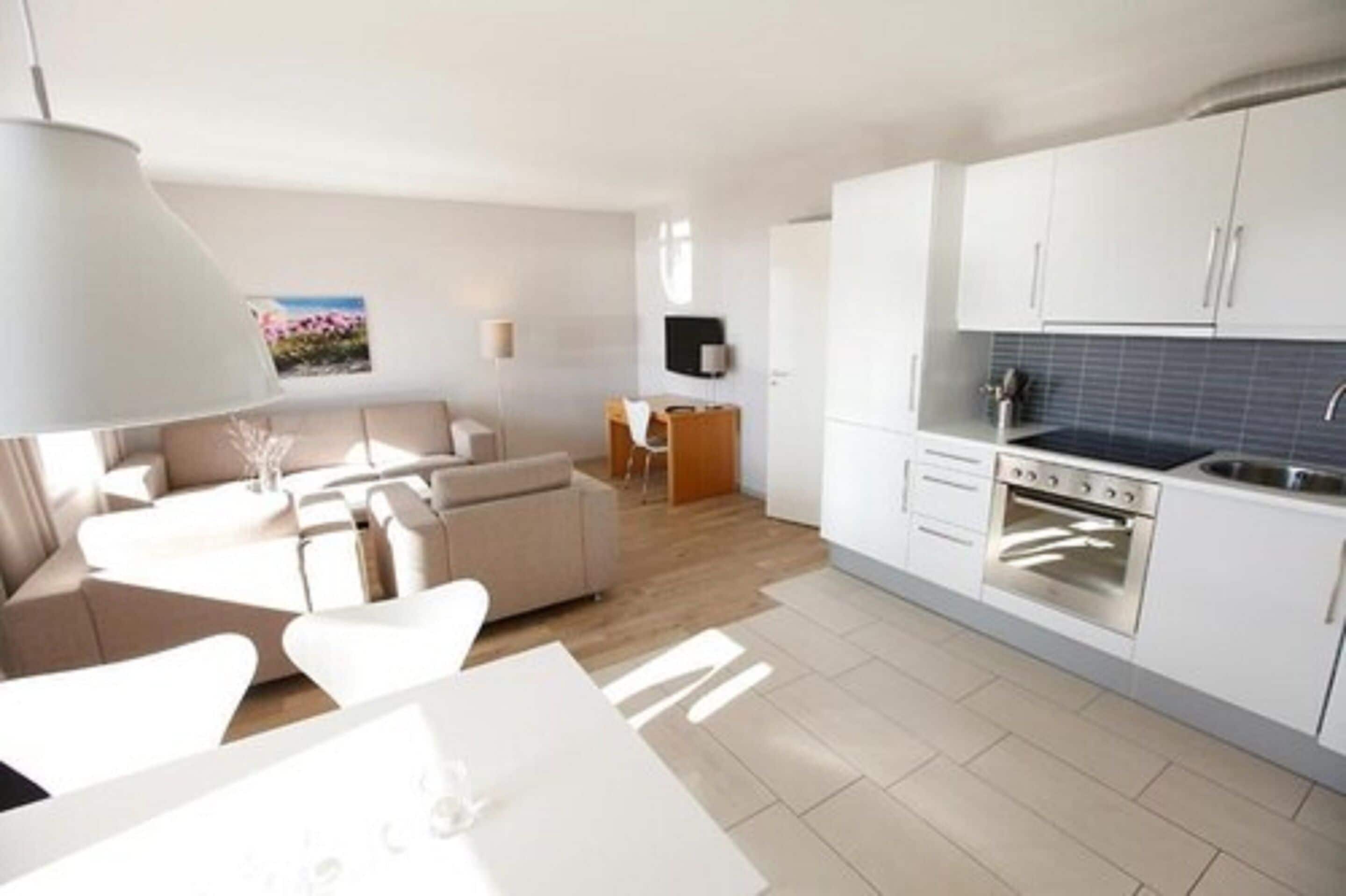 A modern kitchen with white cabinets, a built-in oven, and a dining area with a white table and chairs.
